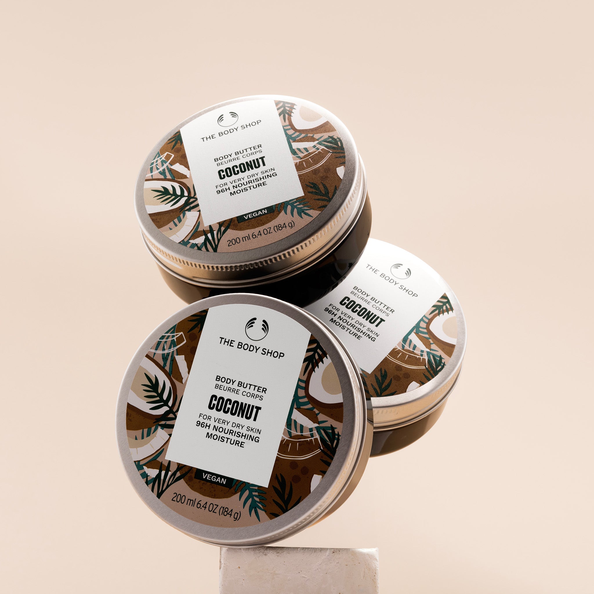 Three containers of The Body Shop Coconut body butter on a beige background