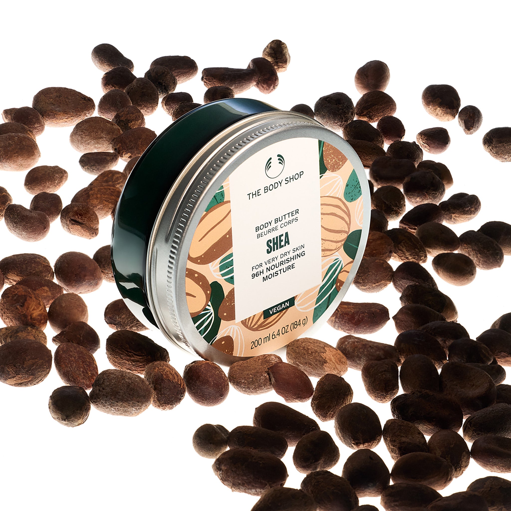 The Body Shop Shea body butter jar surrounded by shea nuts on a white background