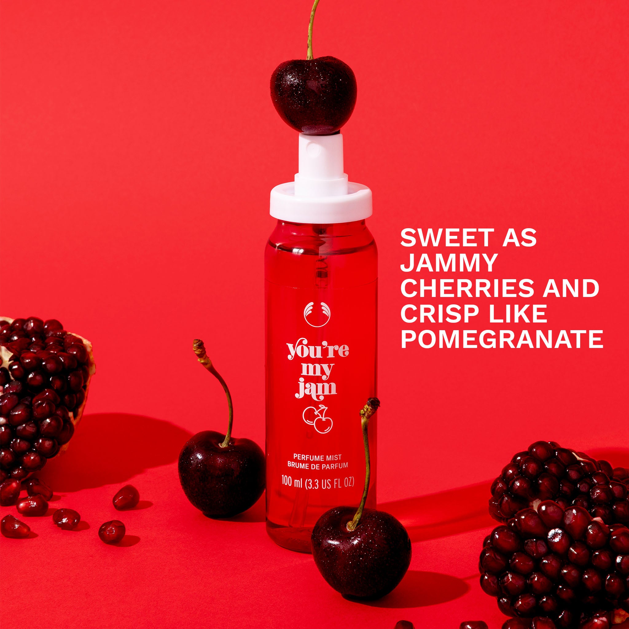 You're My Jam Fragrance Mist - The Body Shop. Bottle against a red background with cherries and pomegranate fruit scattered around the bottle. Overlay text 'Sweet as Jammy Cherries and crisp like pomegranate'.